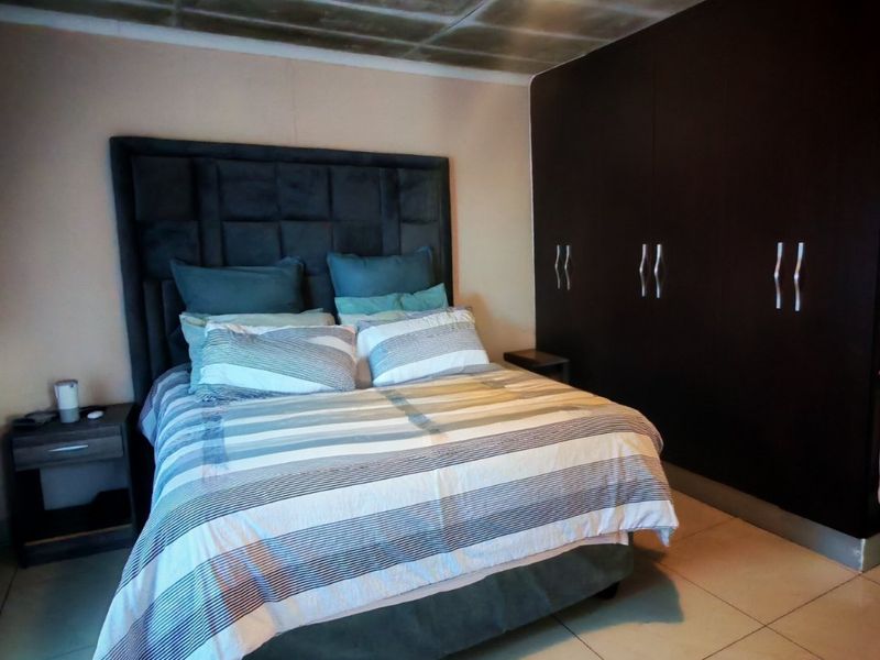 A bedroom featuring dark built-in cupboards, tiled flooring, and a textured ceiling finish.