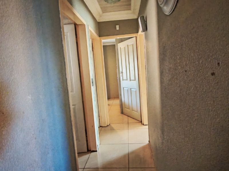 A narrow residential hallway featuring tiled flooring, panel doors, and decorative ceiling molding, requiring cosmetic updates to improve the overall finish.
