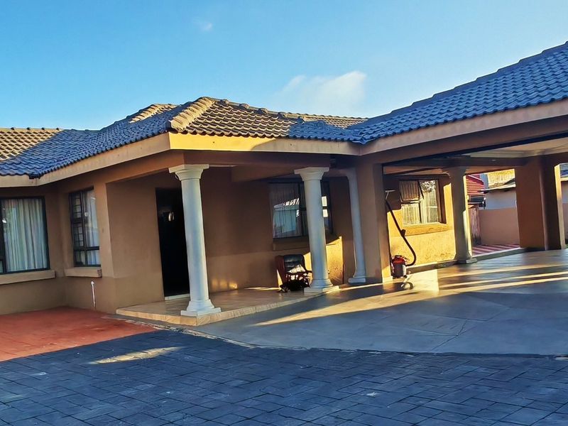 Front elevation of a single-story house featuring a tiled roof, covered carport, and decorative columns with a paved driveway and entrance area.