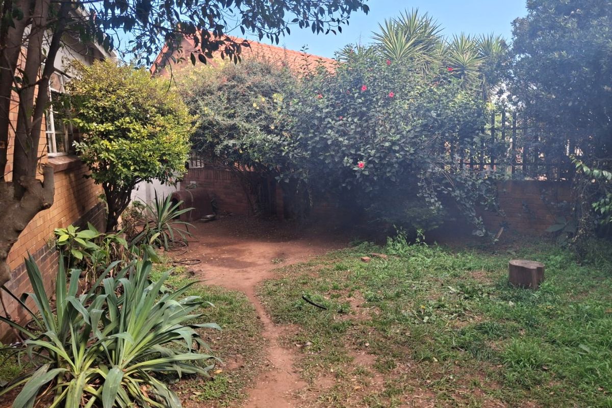 A rear garden area featuring a brick boundary wall, mature shrubs, and a tiled roof section of the main house structure.