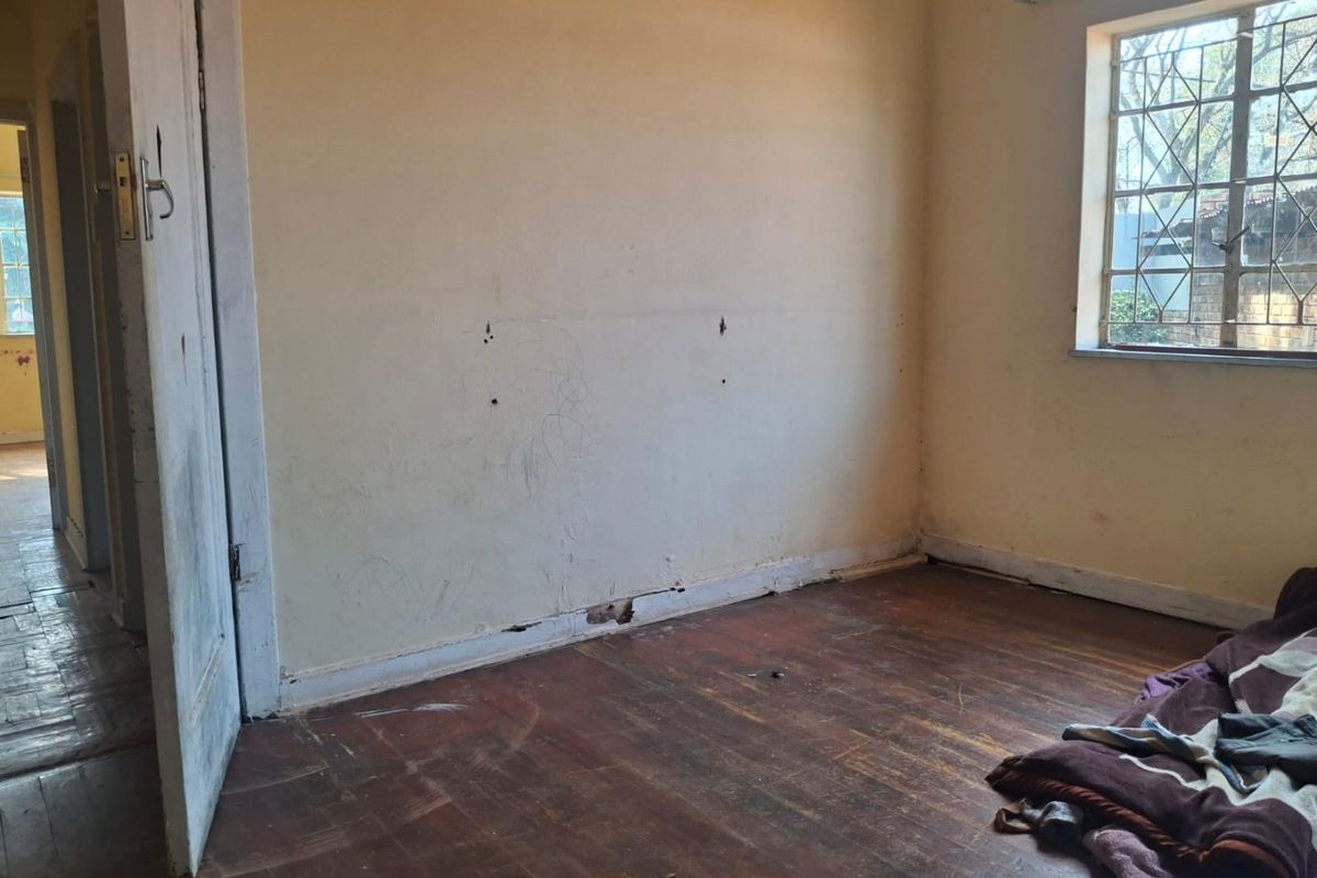 A vacant bedroom featuring original timber flooring, security bars on the window, and walls requiring cosmetic repair and repainting.
