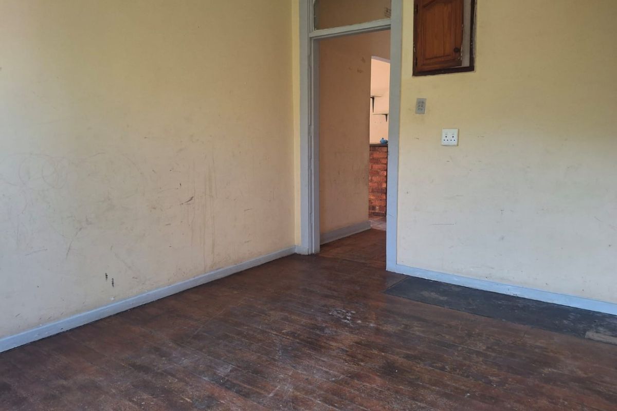 An empty living room featuring worn timber flooring and walls requiring cosmetic attention, providing a blank canvas for renovation and interior updates.