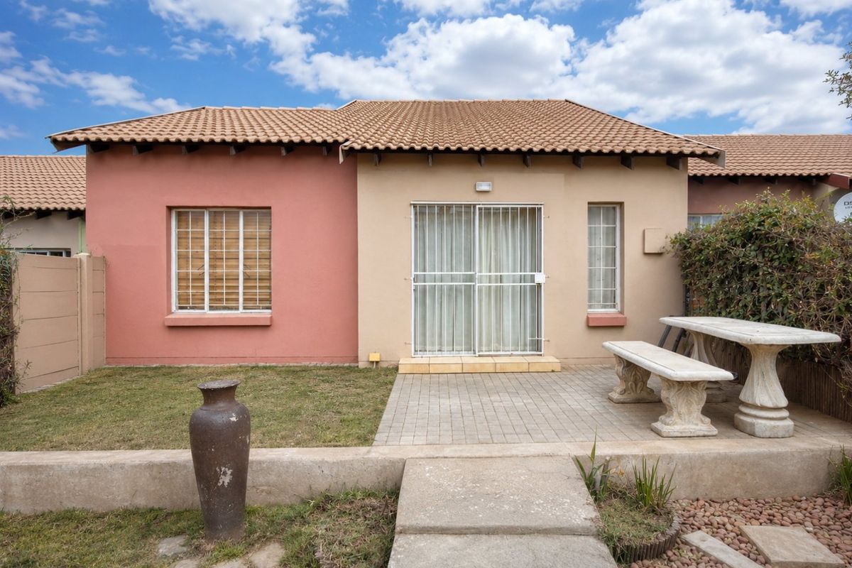 Rear view of the townhouse featuring a paved patio area, sliding glass door with security gate, and a small private garden space.