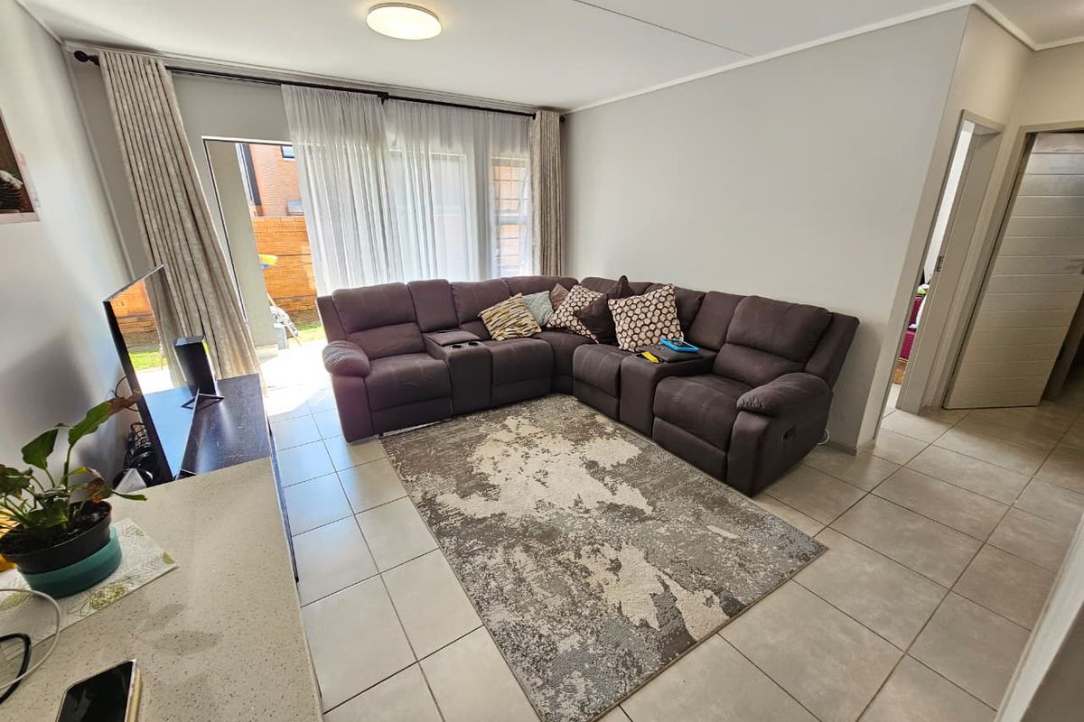 A bright living room featuring neutral tiled flooring and a large sliding glass door providing access to the outdoor area.