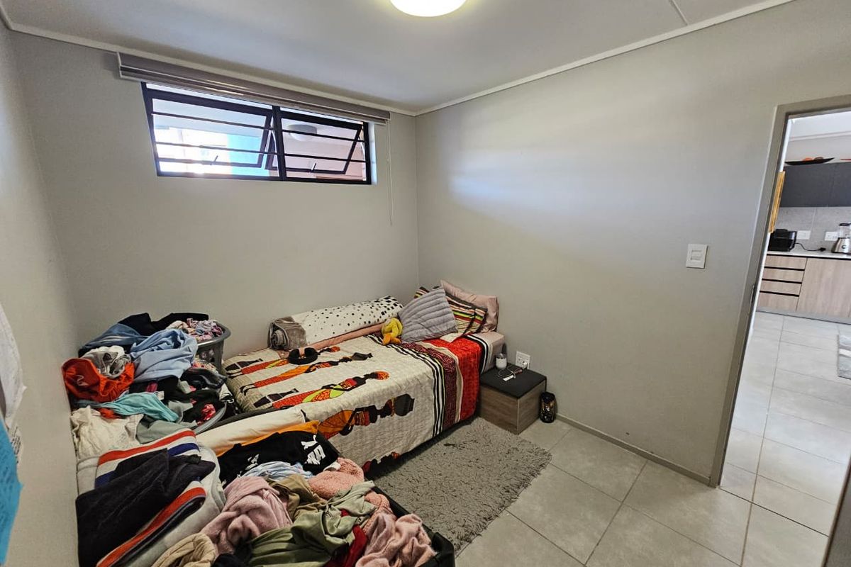 A functional bedroom featuring tiled flooring and a louvre window, with direct access to the adjacent kitchen area.