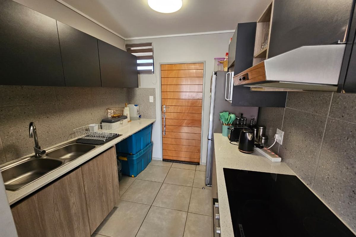 Modern galley-style kitchen featuring stone countertops, double bowl sink, electric hob with extractor fan, and contemporary cabinetry with tiled finishes.