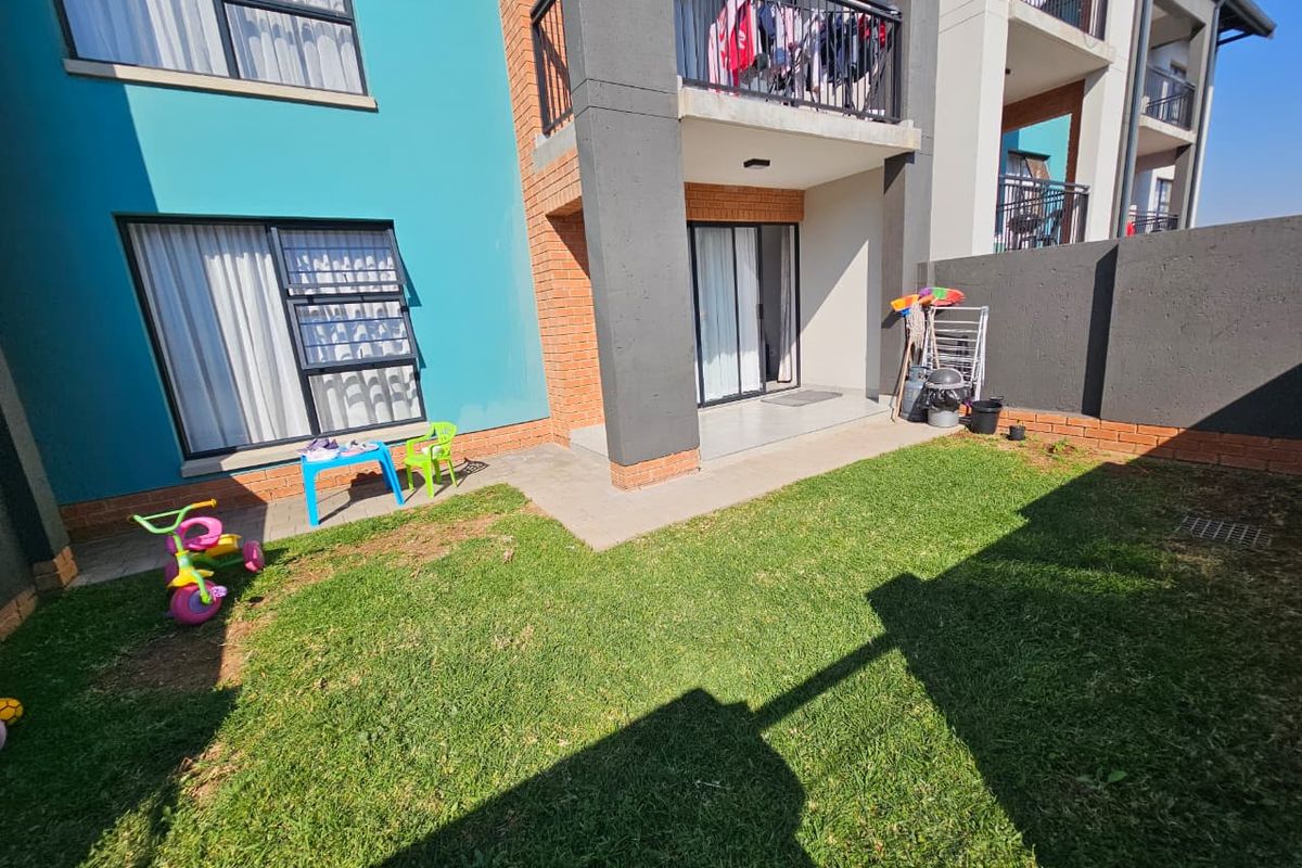 Rear view of the apartment featuring a private garden, paved patio area, and access to the ground floor living space via sliding doors.