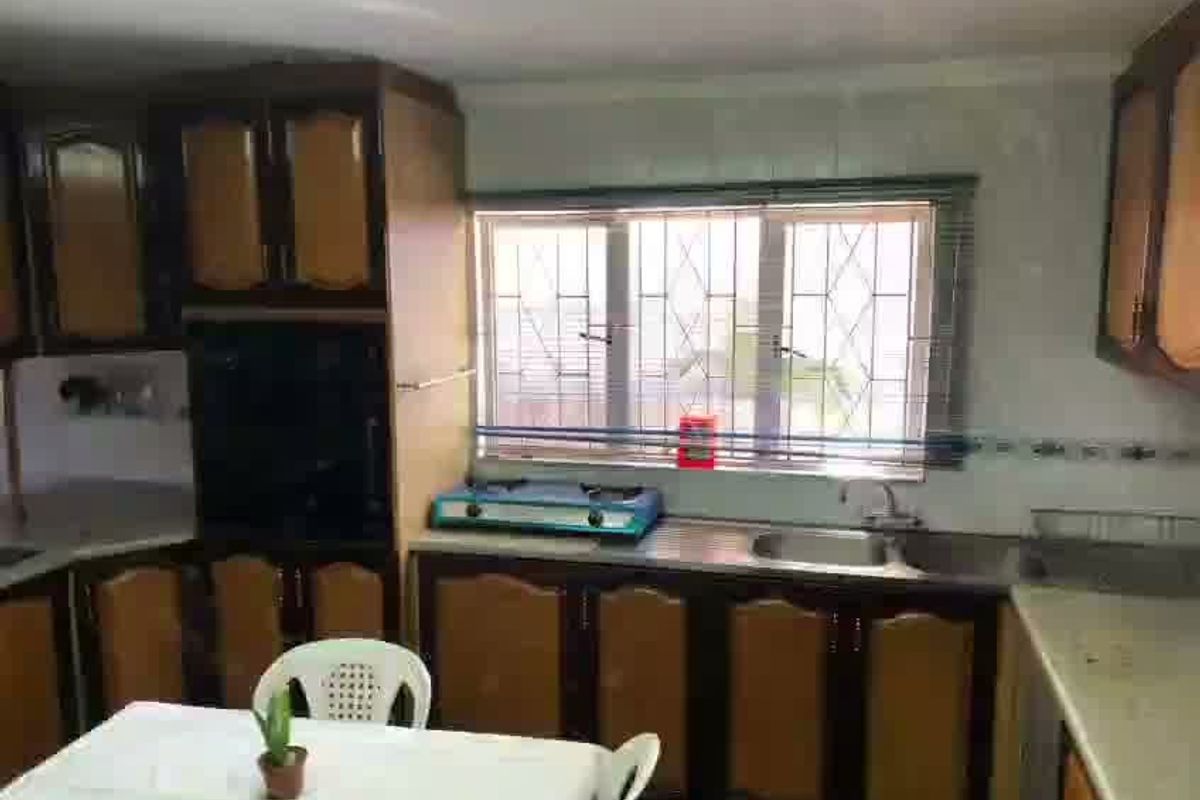 A dated kitchen featuring traditional wood-tone cabinetry, a stainless steel sink, and security bars on the window, offering potential for a modern renovation.