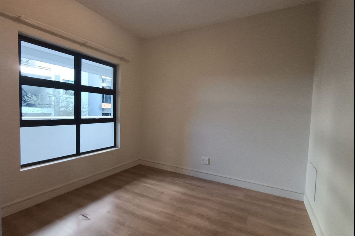 A bright, empty bedroom featuring light-toned laminate flooring and a large aluminium-framed window, providing a clean and neutral space ready for personalization.