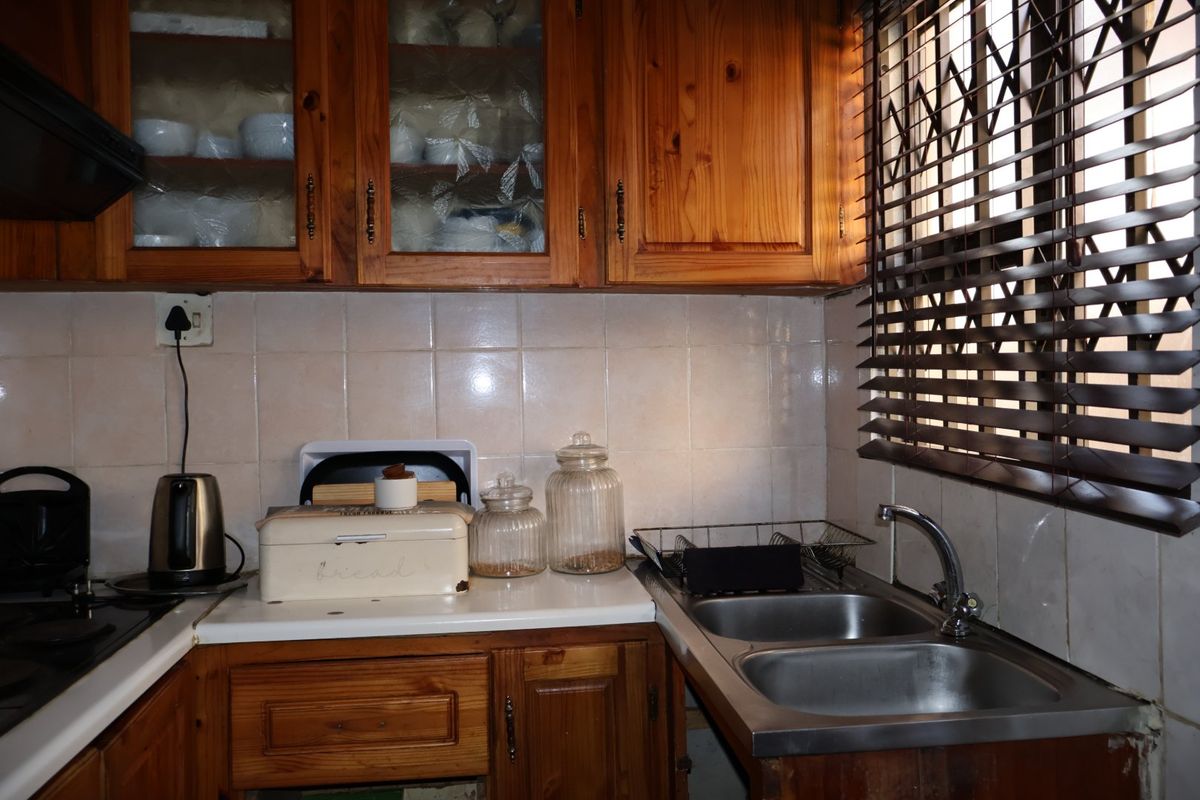 A functional kitchen featuring wooden cabinetry, a double bowl stainless steel sink, and ceramic tile backsplash, showing signs of wear and dated finishes.