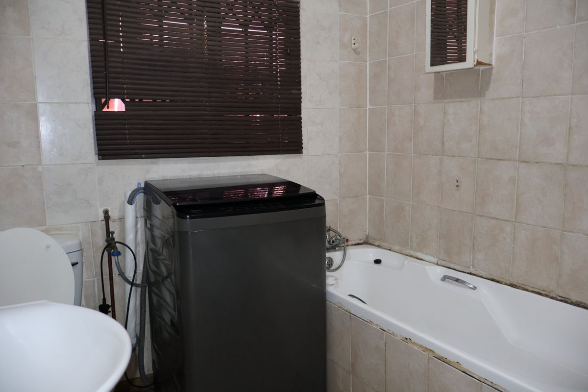 A functional bathroom featuring a bathtub, toilet, and washbasin with tiled walls and window blinds.