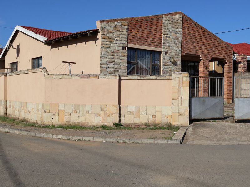 Front exterior view of a single-story house featuring a combination of brick and stone cladding, a tiled roof, and a secure perimeter wall.
