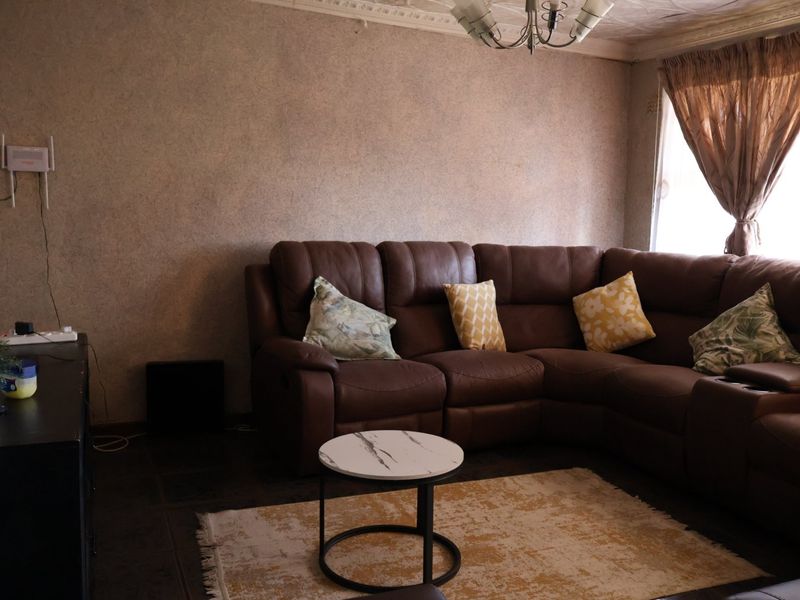 A living room featuring tiled flooring and decorative ceiling cornicing, currently showing signs of wear on the ceiling surface.