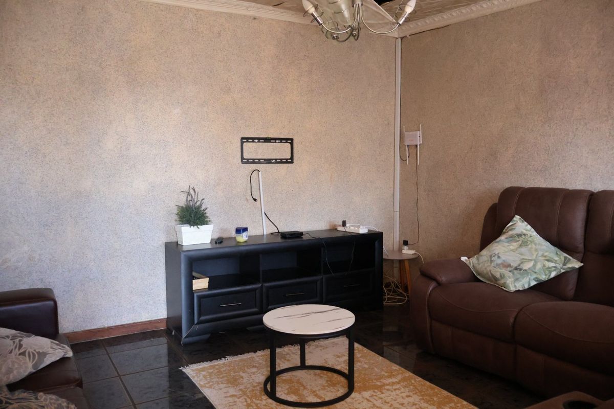 Living room featuring dark tiled flooring, textured wall finishes, and a ceiling rose. The space requires cosmetic updates to the ceiling and wall finishes.
