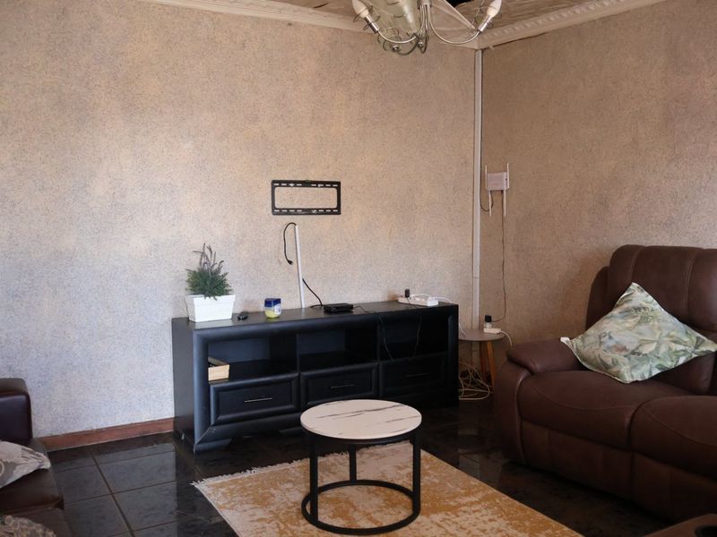 Living room featuring dark tiled flooring, textured wall finishes, and a ceiling rose. The space requires cosmetic updates to the ceiling and wall finishes.