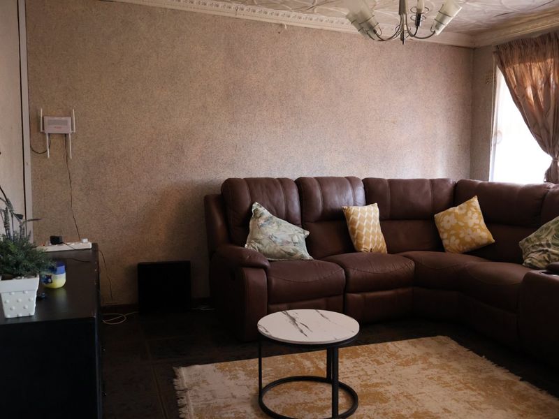 A living room featuring tiled flooring, decorative ceiling cornicing, and textured ceiling finishes, offering a functional space with potential for cosmetic updates.