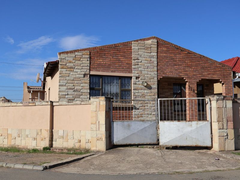 Front elevation of a brick and stone-clad house featuring a secure metal gate, boundary wall, and concrete driveway.