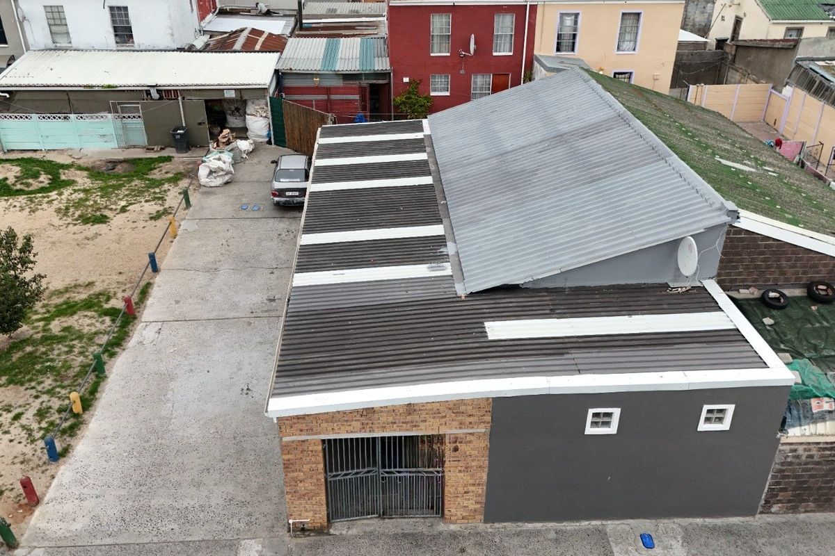 Aerial view of a property featuring a corrugated metal roof, brick and rendered facade, and a concrete driveway with secure gated access.