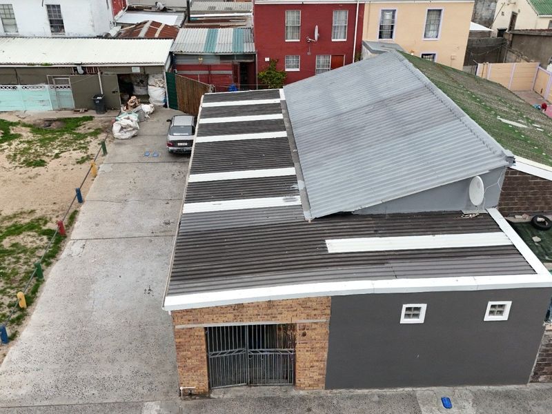 Aerial view of a property featuring a corrugated metal roof, brick and rendered facade, and a concrete driveway with secure gated access.
