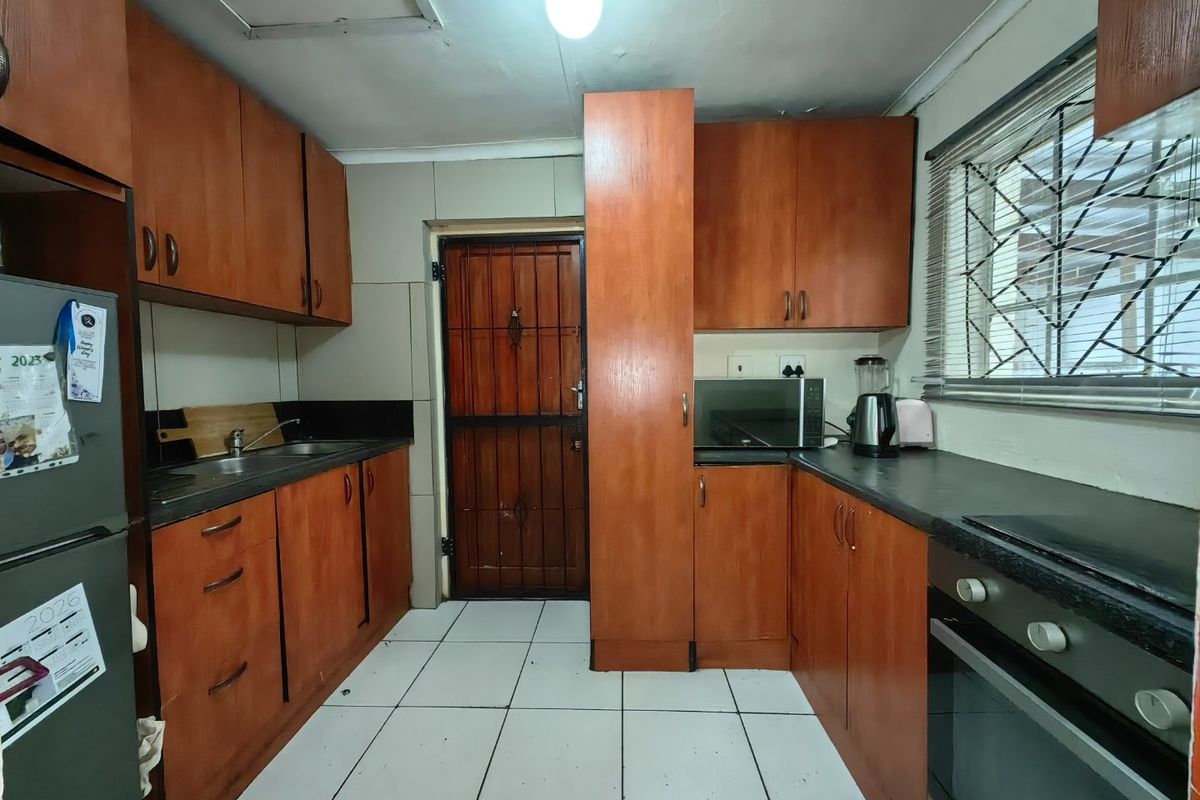 A functional kitchen featuring wooden cabinetry, laminate countertops, built-in oven, and tiled flooring, with direct access to an exterior security door.