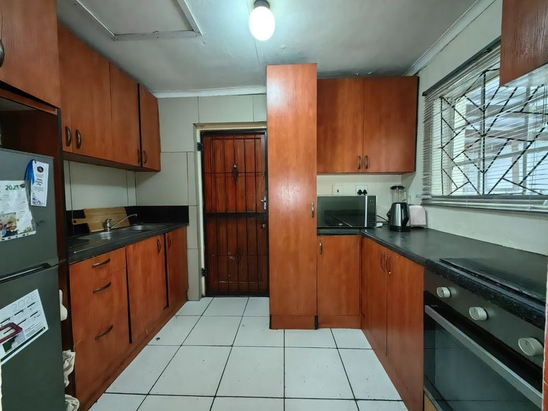 A functional kitchen featuring wooden cabinetry, laminate countertops, built-in oven, and tiled flooring, with direct access to an exterior security door.