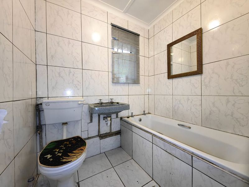 A dated bathroom featuring a standard bathtub, wall-mounted basin, and toilet, finished with full-height marble-effect wall tiling and ceramic floor tiles.