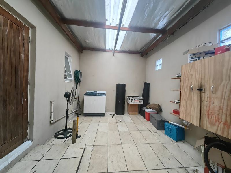 A functional laundry area featuring tiled flooring, exposed timber rafters with translucent roof panels, and built-in storage cabinetry.