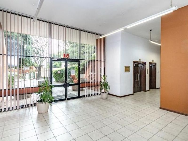 Spacious apartment building entrance lobby featuring tiled flooring, floor-to-ceiling glass frontage, and a double elevator bank for convenient access.