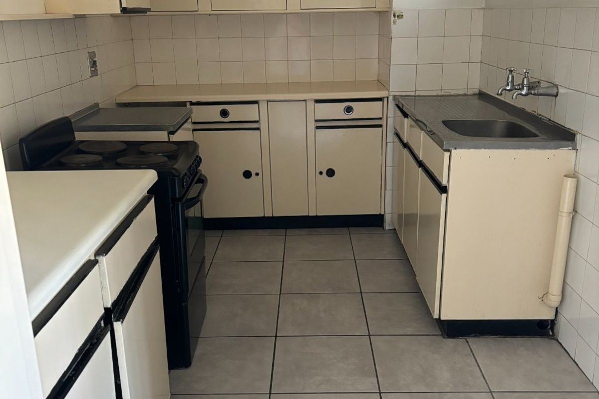 A functional, dated kitchen featuring tiled splashbacks, built-in cabinetry, a stainless steel sink, and ceramic floor tiles.