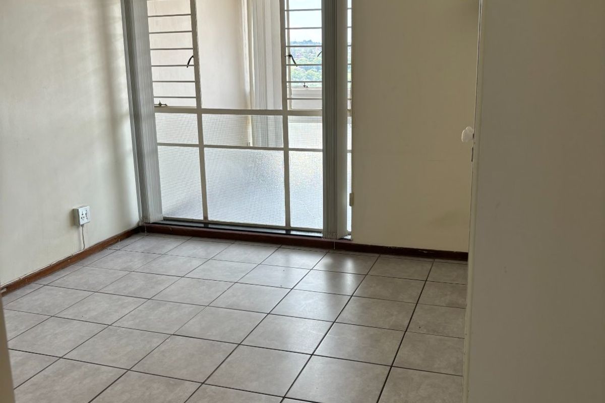 An empty bedroom featuring neutral tiled flooring and a large sliding glass door with integrated security bars, providing access to an outdoor area.