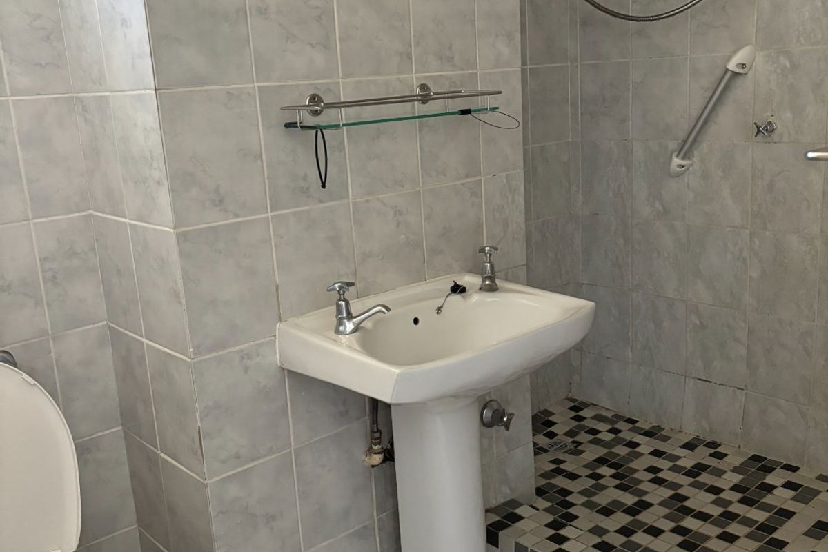 A functional bathroom featuring a pedestal basin, toilet, and a tiled shower area with a raised step. Requires minor repairs to fixtures.