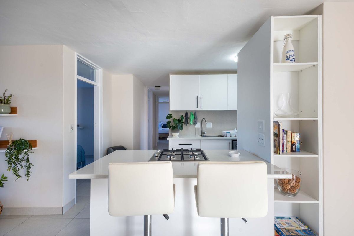 Modern kitchen featuring a central island with a built-in gas hob, white cabinetry, stone countertops, and integrated shelving.