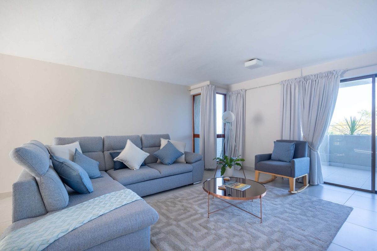 A bright and well-maintained living room featuring neutral tiled flooring and direct access to an outdoor balcony through sliding glass doors.