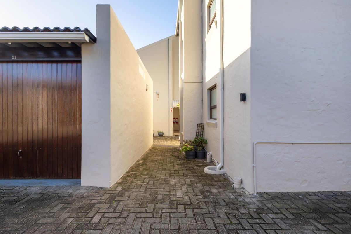 A paved exterior walkway between apartment building walls, featuring a garage door and external drainage infrastructure.