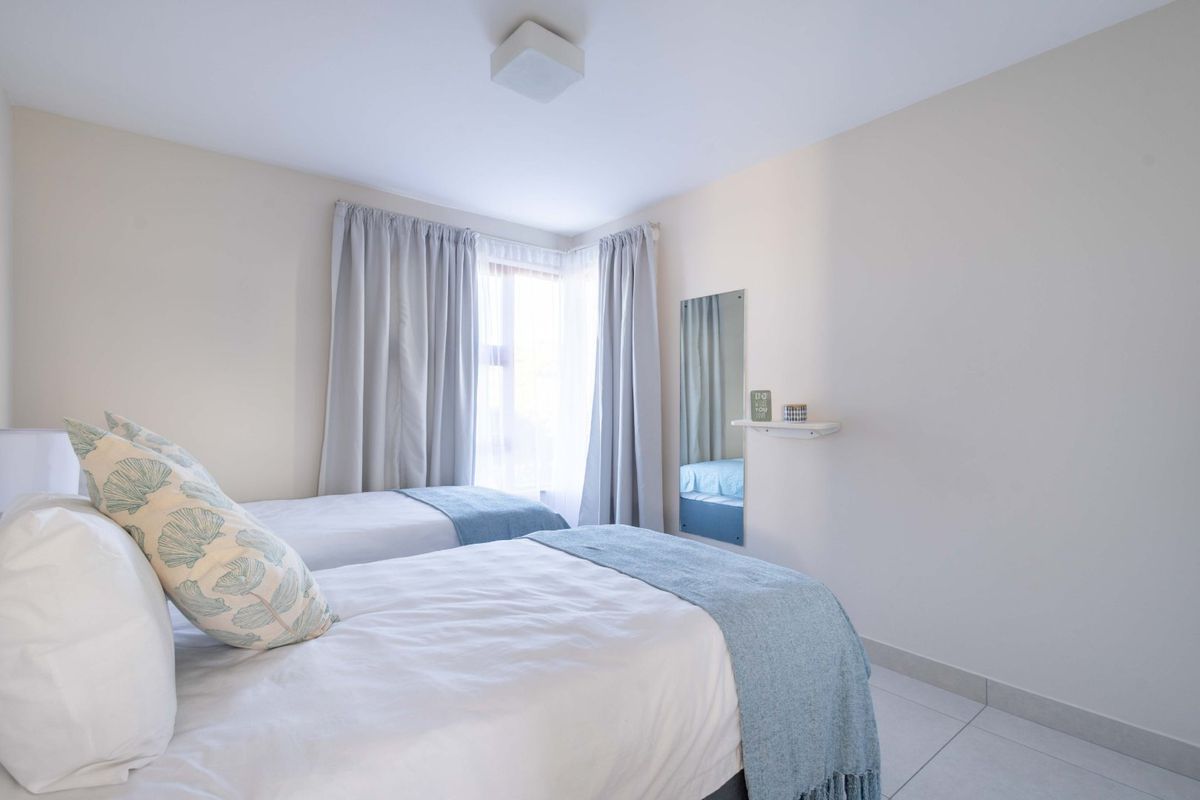 A bright and tidy bedroom featuring tiled flooring, neutral walls, and a wall-mounted mirror with a small shelf.
