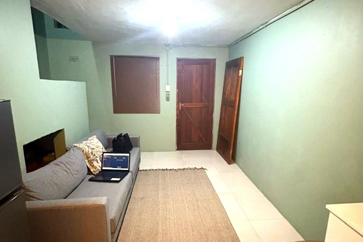 A simple living area featuring tiled flooring, a timber door, and surface-mounted electrical conduit along the ceiling.