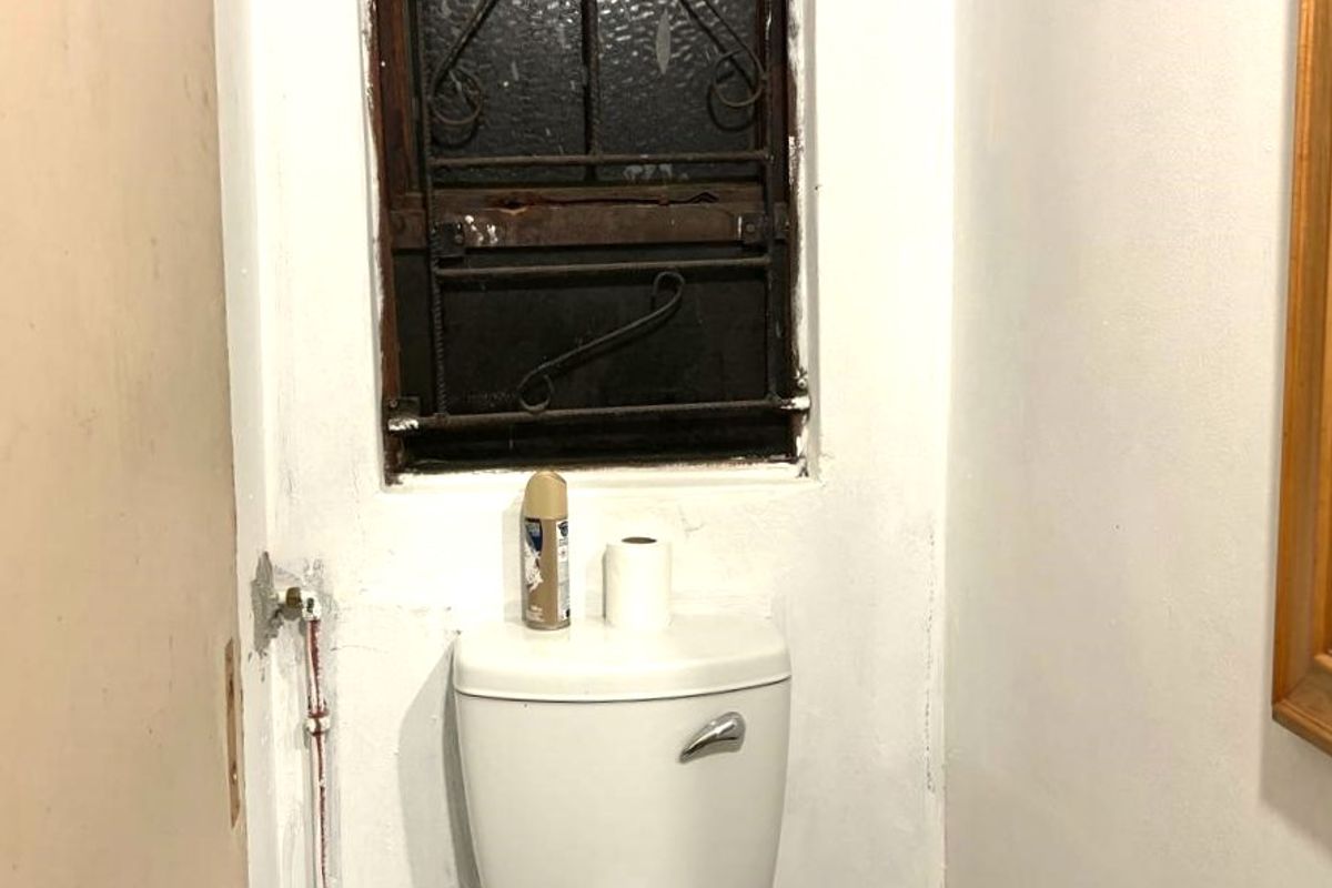 A small bathroom featuring a toilet and sink, requiring cosmetic updates and maintenance to the window frame and exposed plumbing.