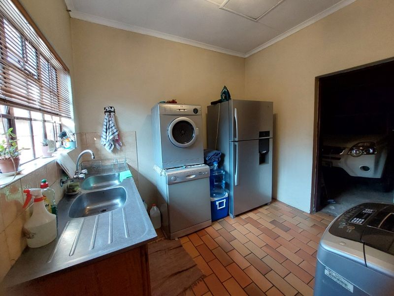 A functional laundry room featuring a double stainless steel sink, tiled flooring, and direct access to the garage area.