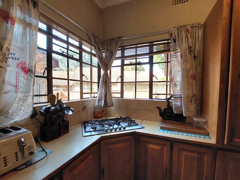 A functional corner kitchen featuring wooden cabinetry, a built-in gas hob, tiled backsplash, and ample natural light from corner windows.
