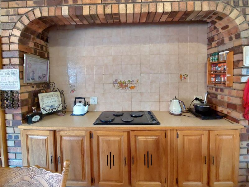 A kitchen area featuring a distinctive brick archway, tiled backsplash, electric hob, and traditional wooden cabinetry.