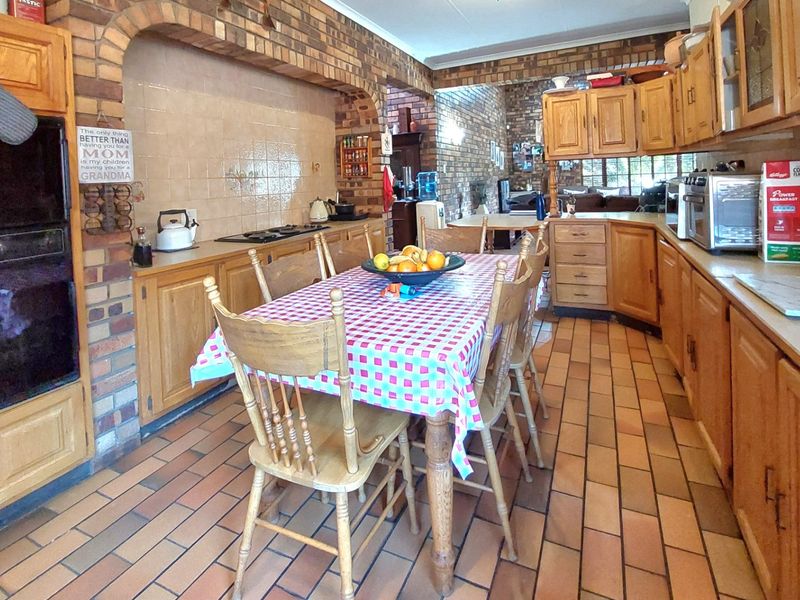 Open-plan kitchen and dining area featuring rustic brick archways, traditional wooden cabinetry, gas hob, built-in oven, and durable tiled flooring.