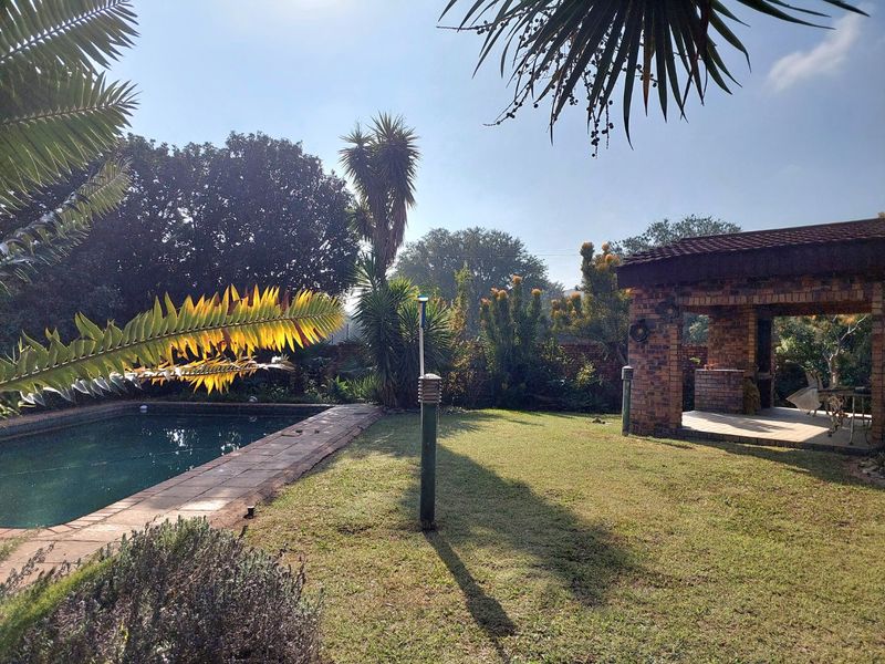 A well-maintained outdoor entertainment area featuring a swimming pool, paved surround, and a brick-built lapa with a built-in braai.