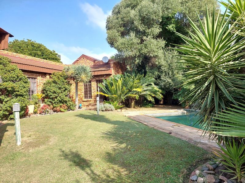 Rear garden view featuring a swimming pool, paved surround, and established landscaping against a face-brick house exterior.
