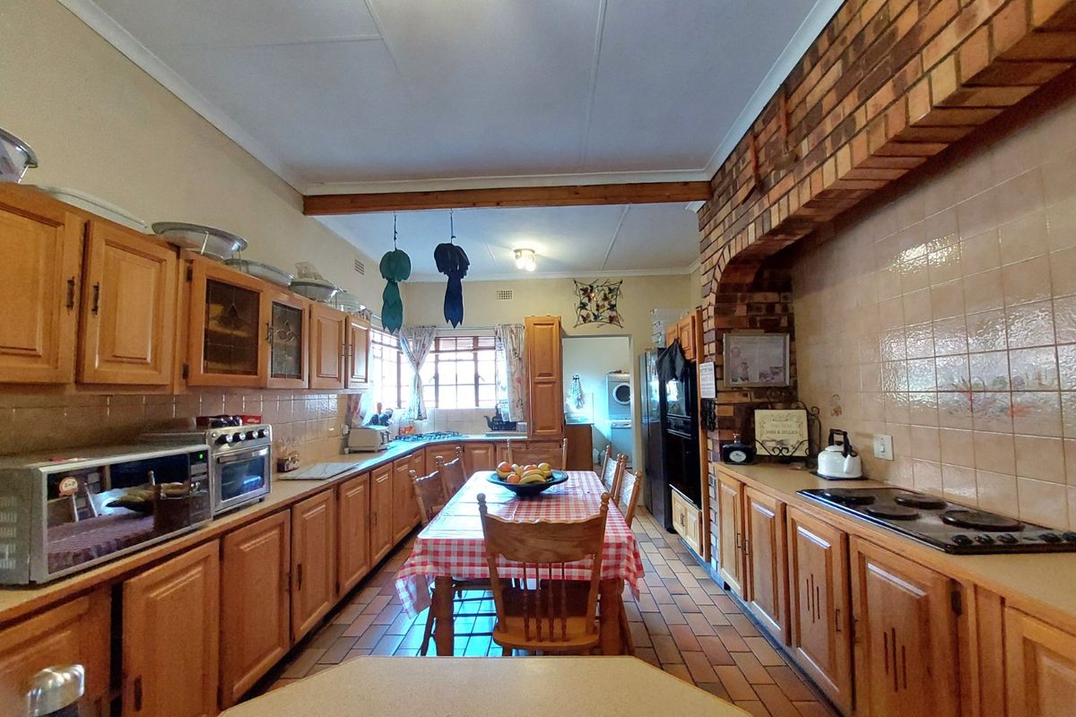 Spacious kitchen featuring traditional wooden cabinetry, a brick feature wall, tiled backsplash, and integrated cooking appliances with a central dining area.