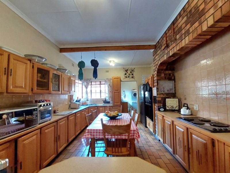 Spacious kitchen featuring traditional wooden cabinetry, a brick feature wall, tiled backsplash, and integrated cooking appliances with a central dining area.