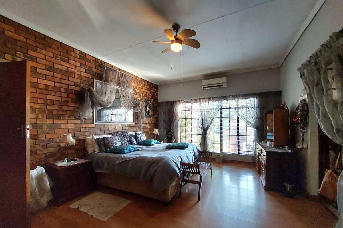 Spacious bedroom featuring an exposed brick accent wall, laminate flooring, ceiling fan, and a wall-mounted air conditioning unit.