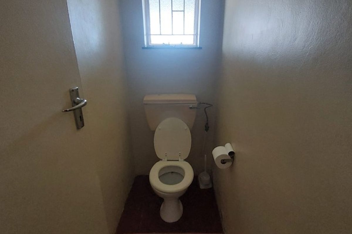 A compact, functional guest toilet featuring a standard white toilet suite and a small window with security bars.