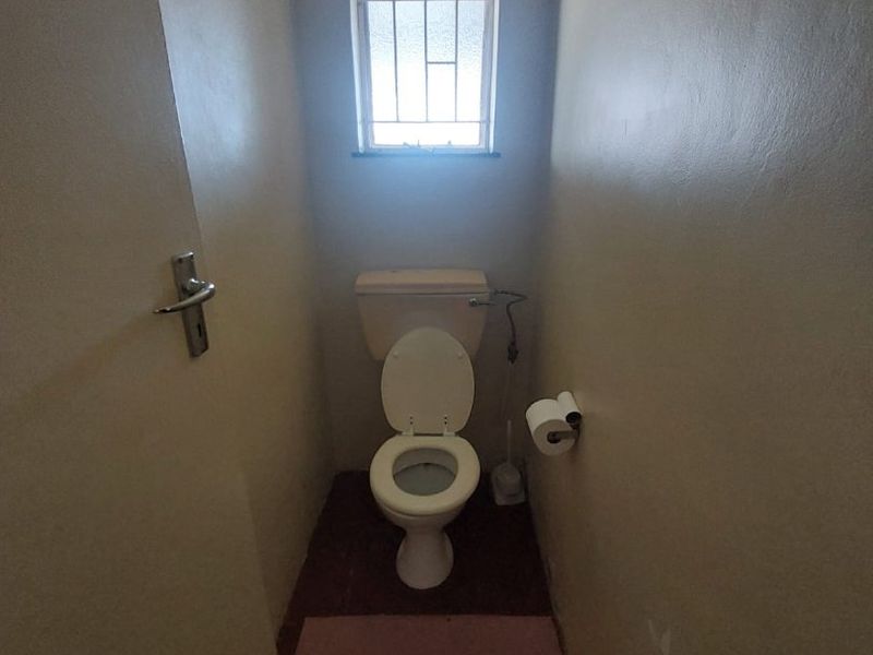 A compact, functional guest toilet featuring a standard white toilet suite and a small window with security bars.
