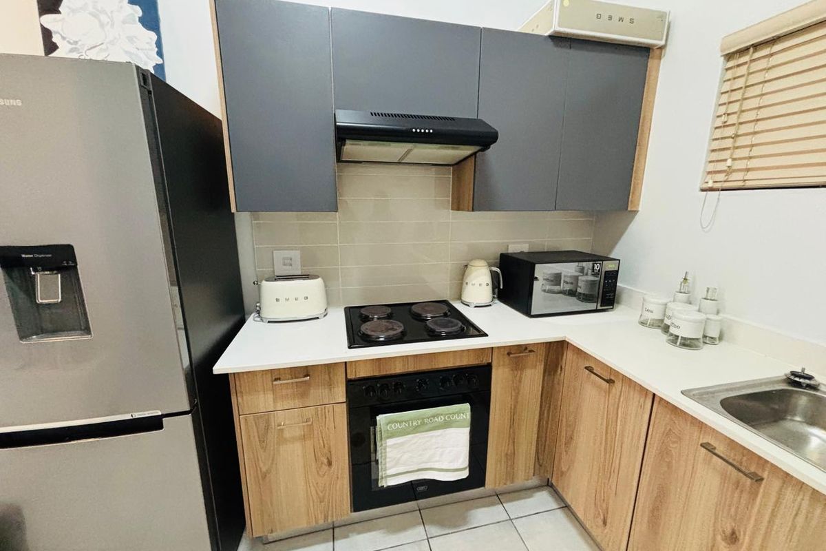 Compact modern kitchen featuring wood-grain lower cabinetry, dark grey upper cupboards, stone countertops, and integrated electric cooking appliances.