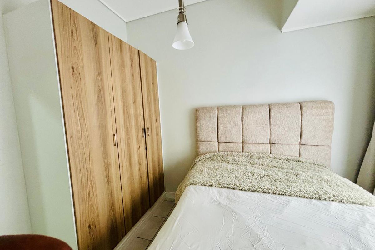 A bedroom featuring a built-in wooden wardrobe and a modern pendant light fixture.